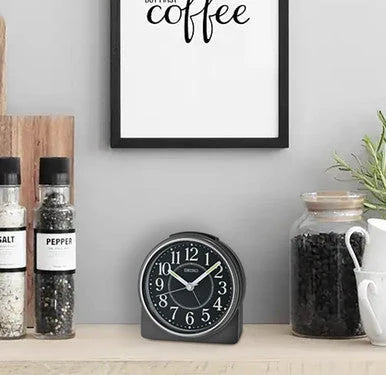 Seiko QHE198KLH black alarm clock styled on a shelf beside coffee jars